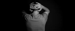 person with hands clasped behind head back turned to camera black and white