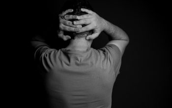 person with hands clasped behind head back turned to camera black and white