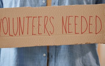 person holding cardboard sign volunteers needed