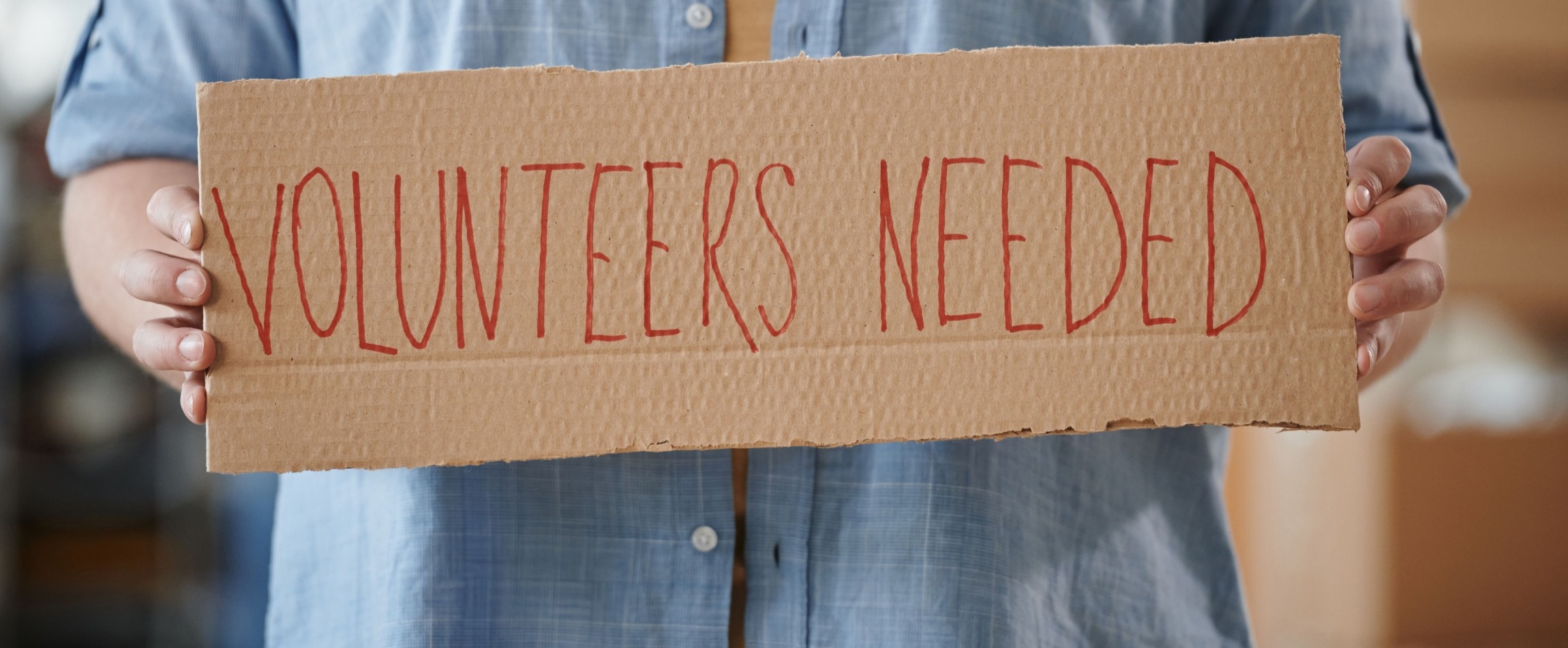 person holding cardboard sign volunteers needed
