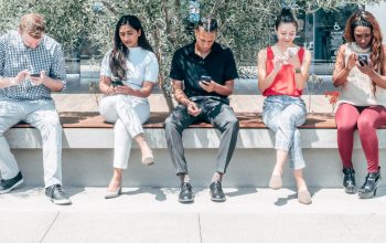 row of people looking at smartphones outdoors